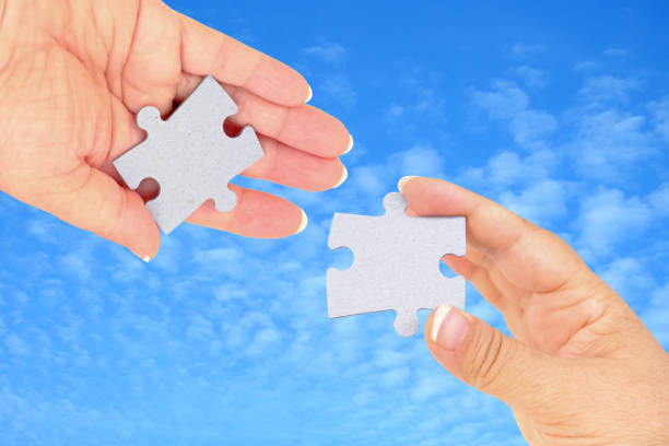 istock Two hands trying to connect couple puzzle piece on background. Teamwork concept. Closeup hand of connecting jigsaw puzzle 1857182507