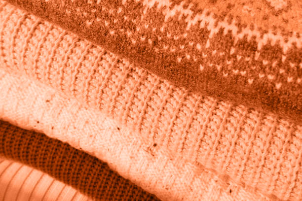 stack of warm sweaters, wool jumpers peach color Color year 2024, geometric pattern, concept gentle washing and care of knitwear, new purchase, fashionable clothes