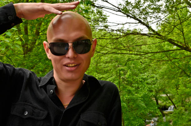 Half portrait of a caucasian man in his 30s with a shaved head and wearing glasses. Portrait taken outdoors and is a self portrait