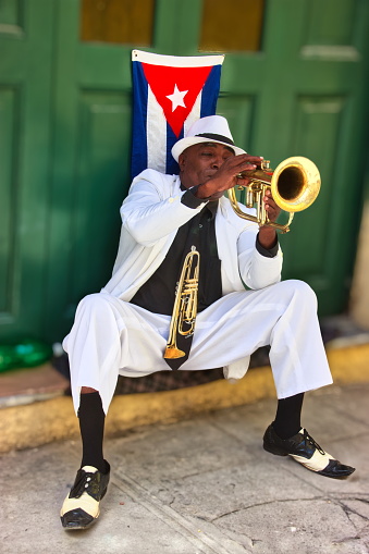 Havana, Cuba - April 08,2016 :  Cuban street musician dressed in white suit,  playing the trumpet in front of a green door and at a street in old Havana