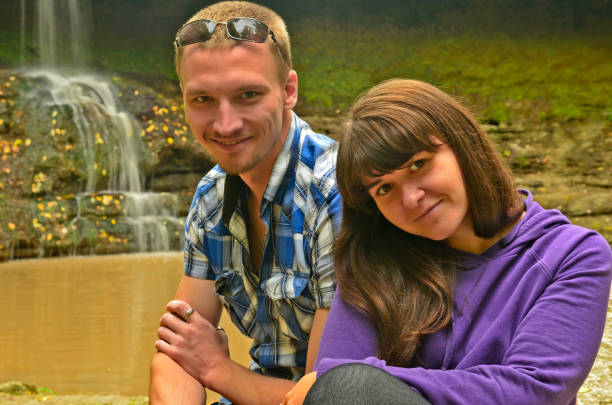 Close up on a Caucasian couple holding hands by the river, showcasing the engagement ring on the woman's hand by the river.