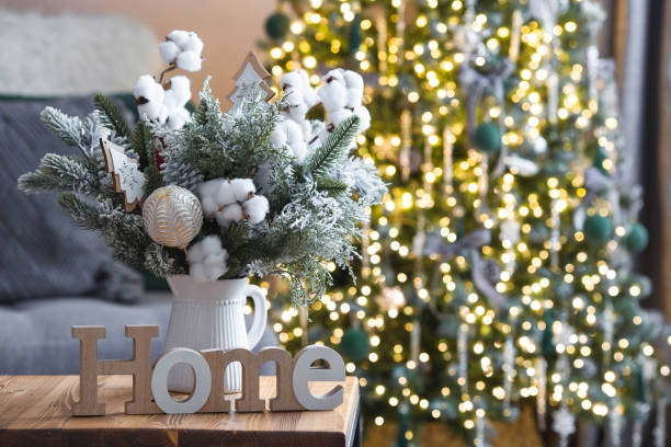 a bouquet of fir trees with cotton and toys and a home sign on the table against the background of christmas tree garlands. winter decorations in the interior. the concept of new year holidays 2024. - christmas tree branch imagens e fotografias de stock