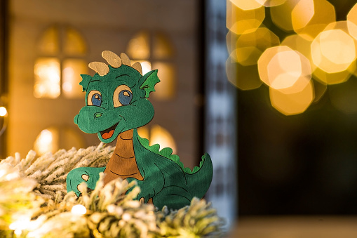 Zodiac sign. A New Year's toy in the form of a green wooden dragon on the background of a garland and a beautiful bokeh. Glowing Christmas holiday background. Chinese horoscope for 2024.