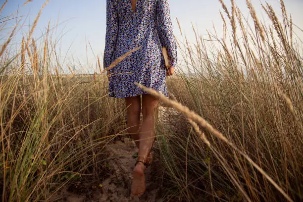 Young woman wearing a flower blue dress walking in the sand dunes holding a book in her hands