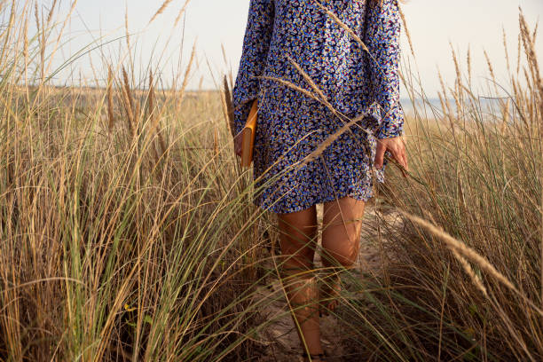 Young woman wearing a flower blue dress walking in the sand dunes holding a book in her hands