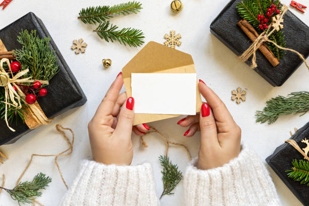 istock Hands with card and envelope near gift boxes, fir branches and Christmas decor, Mockup 1857349307