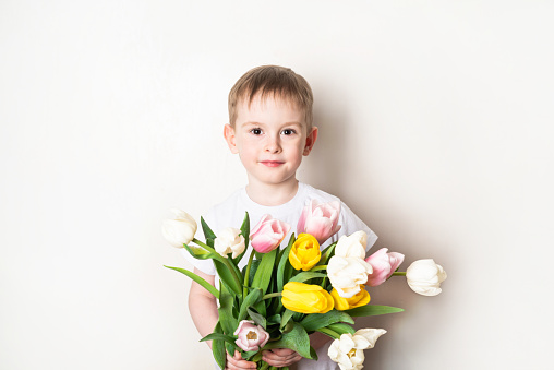Portrait of a smiling boy with freckles in a white t-shirt with a bouquet of tulips on a white background.