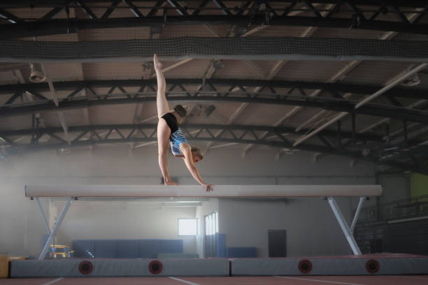 Female gymnast performing on balance beam during practice in sports hall.