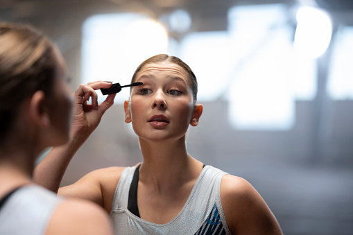 Gymnast young woman applying eyelash makeup while looking at mirror.
