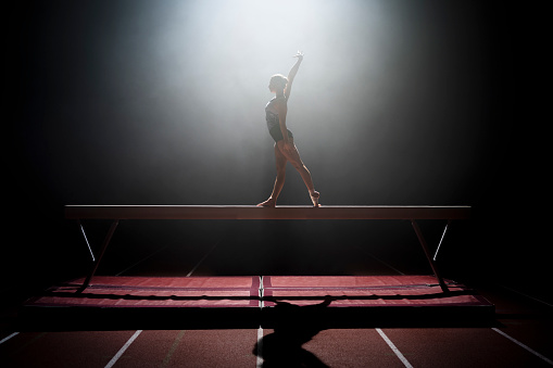 Female gymnast performing on balance beam during practice in sports hall.
