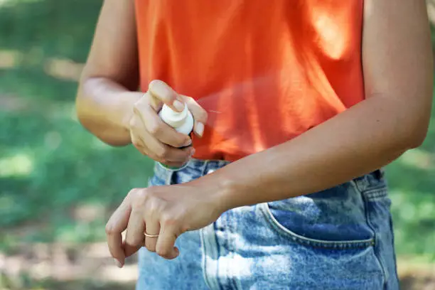 Girl spraying insect repellent on her arm outdoor in nature using spray bottle. Mosquito repellent. Bug spray anti insects.