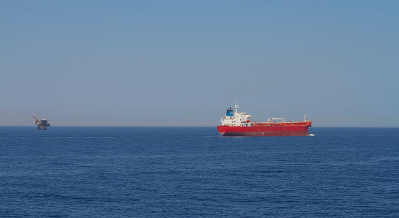 View of the stern of a merchant ship carrying crude oil is underway at sea in calm weather , an oil drilling unit is also visible in the background