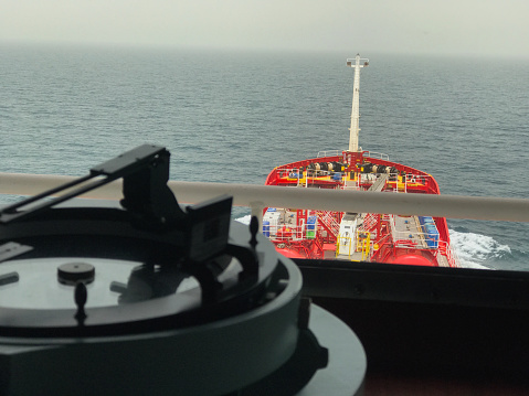 A merchant ship carrying product is underway at sea, blurred view of azimuth circle in the foreground.