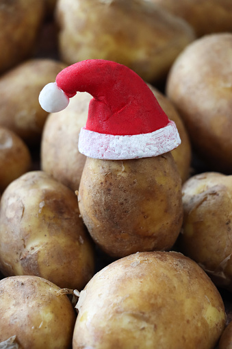 Stock photo showing close-up view of some raw potatoes mounded up high and waiting to be prepared for cooking.  A Santa hat has been added to one potato to a provide a touch of humour. Fun way to encourage healthy eating in children.