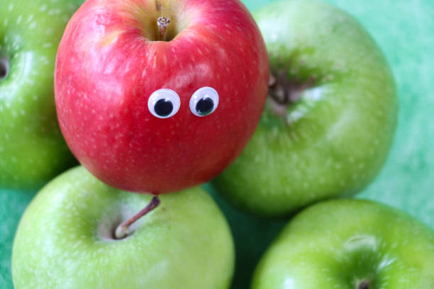 緑のグラニースミスリンゴのグループの上にグーグルの目を持つ赤いリンゴから作られた漫画のキャラクターのクローズアップ画像、果物の光沢のある、斑点のある皮の部分、まだらの緑の� - shiny group of objects high angle view close up ストックフォトと画像