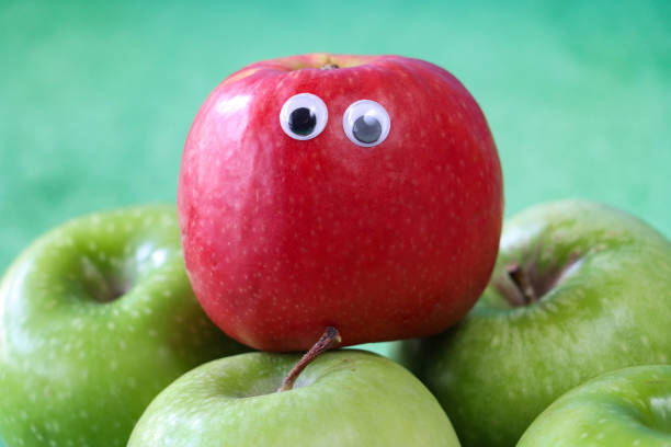 緑のグラニースミスのリンゴのグループの上にグーグルの目を持つ赤いリンゴから作られた漫画のキャラクターのクローズアップ画像、果物の光沢のある、斑点のある皮の部分、まだらの緑� - shiny group of objects high angle view close up ストックフォトと画像