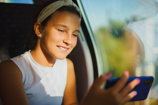 Little smiling girl travels by train while communicating via video conference on phone, takes selfie blog.