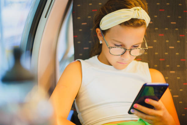 istock Small beautiful girl in glasses sits on train, using her phone 1857442619