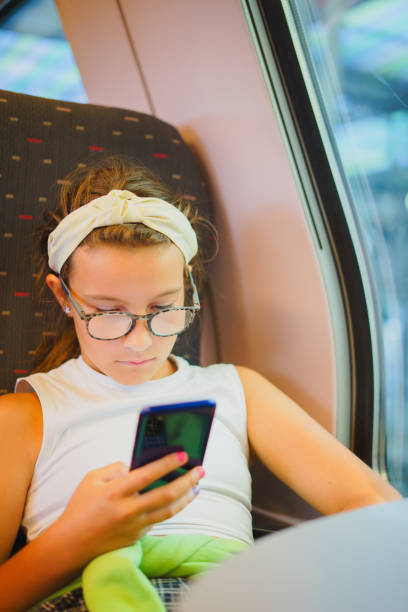 istock Small beautiful girl in glasses sits on train, using her phone 1857443134