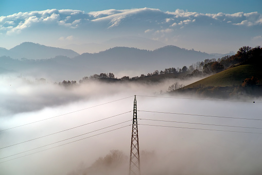 Electricity pylon in the fog against a landscape of hills and mountains