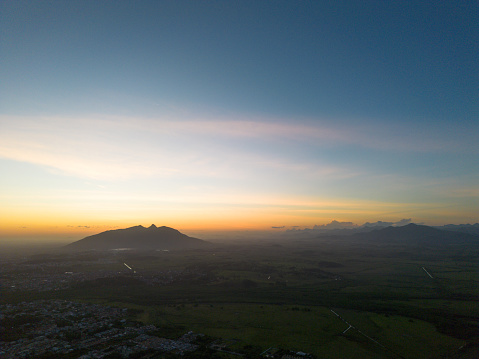 aerial photography taken in Brazil during the evening capturing the sunset behind a lone hill with orange clouds and blue sky