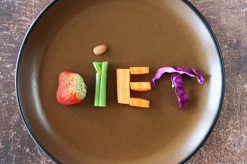 Stock photo showing close-up, elevated of a healthy eating and diet concept depicted by a plate containing fruit and vegetables used to form the letters of the word 'diet'. The letter 'D' is made using a strawberry, a celery stick and almond nut form the 'I', a chopped carrot creates an 'E' whilst shreds of red cabbage are the 'T'.