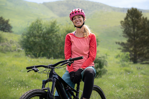 Mature mountain biker resting with electric bicycle in meadow.