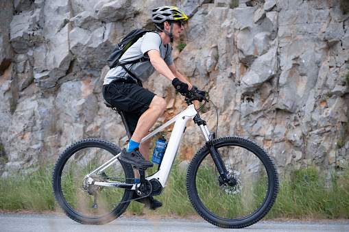 Mid adult man riding electric bicycle on mountain road.