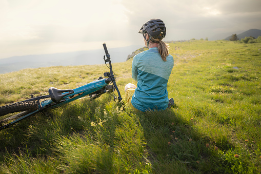 Mature woman sitting with electric bike on mountain top.