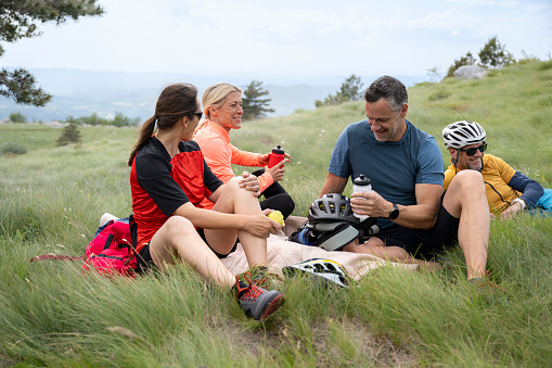 Mature couples talking and relaxing on grassy hill while doing mountain biking.