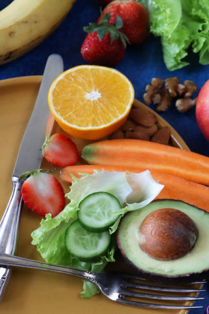 istock Full frame image of yellow plate with stainless steel knife and fork forming clock face and hands, display of healthy nuts, fruit and vegetables on blue background, elevated view, diet and intermittent fasting concept 1857452697