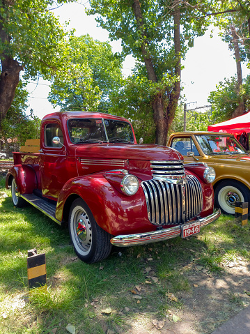 Remedios de Escalada, Argentina - Dec 10, 2023: old red shiny 1946 Chevrolet Chevy AK series 250 pickup truck in a park on the lawn under the trees at a classic car show.