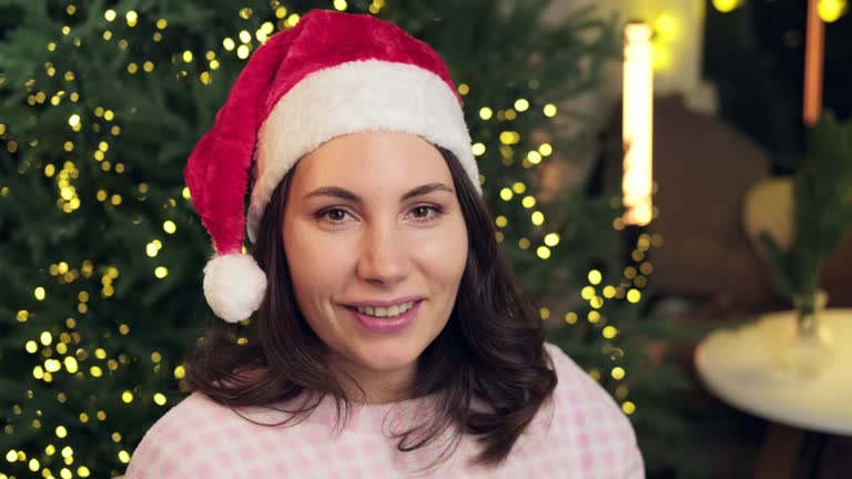 A young attractive woman in a red Christmas hat and pajamas smelling the aroma of hot coffee and looks at the camera close up