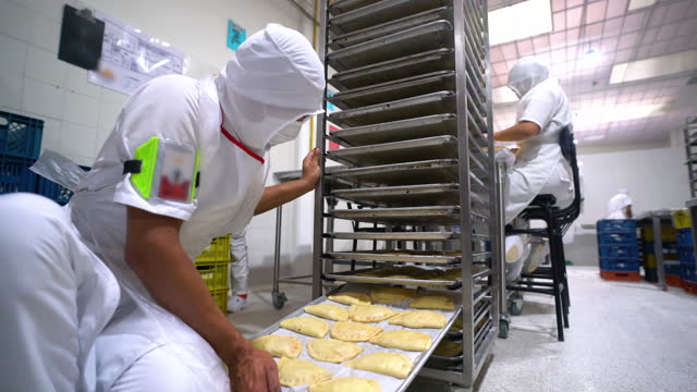 Unrecognizable male employee checking the trays of empanadas on rack before putting them in the oven at a food processing plant