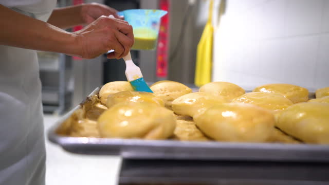 Latin American employee brushing empanadas with egg wash before putting them in the oven at a food processing plant