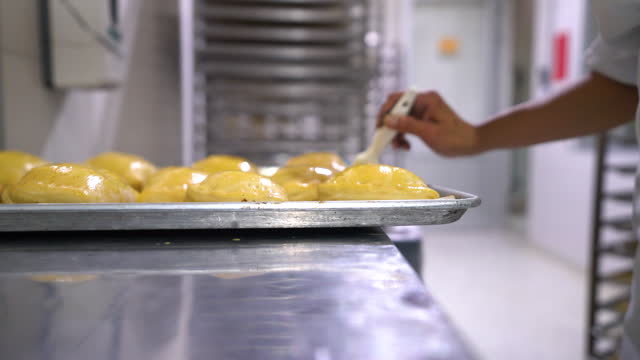 Unrecognizable female employee brushing empanadas with egg wash at a food processing plant