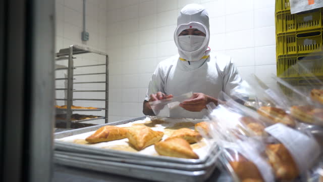 Unrecognizable male employees packing empanadas in individual plastic bags at a food processing plant