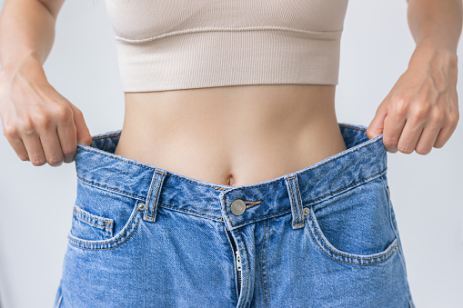 A young woman tries on jeans after a healthy weight loss, shows how big they turned out to be after. The concept of a healthy lifestyle and proper nutrition.