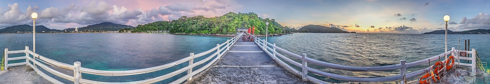 Panoramic picture over a jetty with wooden railing over the tropical sea near Patong on Phuket in the evening