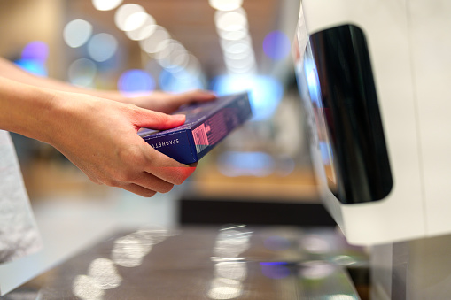 A woman's hands are shown scanning a box of spaghetti at the grocery store's self-checkout service, highlighting the convenience of modern shopping technology.