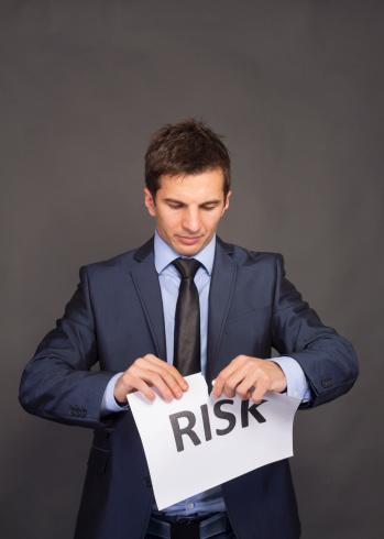 Businessman tearing paper which written risk word.Isolated on Gray