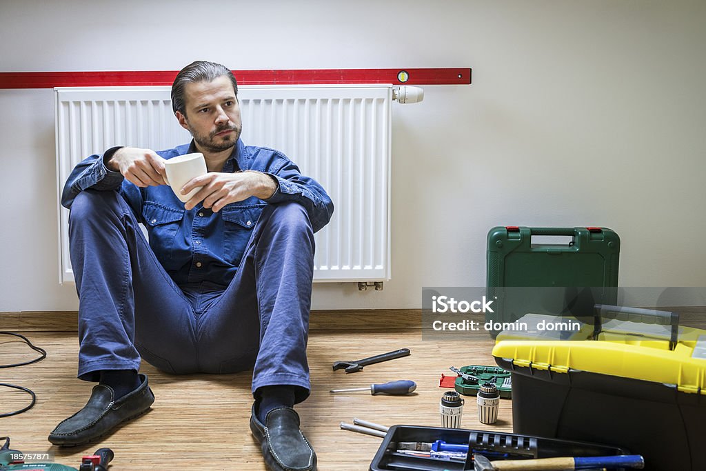 Plombier de travail, la fatigue, les pauses-café, assis sous le chauffage - Photo de Installer libre de droits