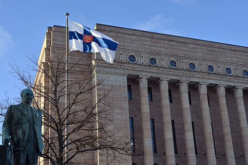 the monument to third president of Finland Pehr Evind Svinhufvud, waving Finnish flag and Finnish parliament building on Finnish Independence Day December 6, 2023