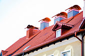 The roof of a residential building, with a tiled roof, a chimney, steps and skylights. The texture of the plaster of a large chimney. Banner with Red tiles and dormer windows