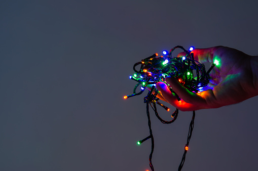 close up of male hand holding tangled christmas string lights with dark background