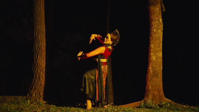 an Asian woman is dancing energetically between two trees with yellow lights