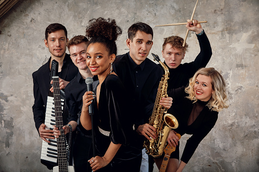 Portrait of diverse group of young people musical band playing with instruments - on gray concrete background.
