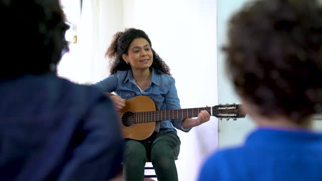 Cheerful Latin American teacher playing a guitar during class with her students looking very happy