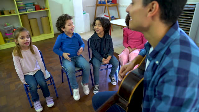 Diverse group of kids having fun during music class while male teacher plays the guitar