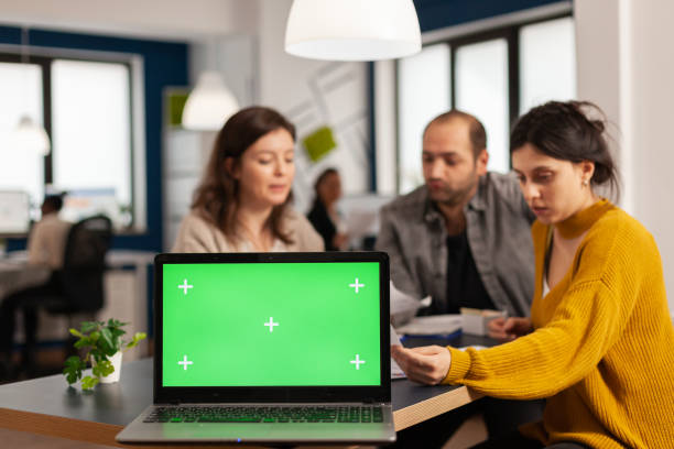 istock Laptop with green screen placed on desk while people work in background 1857779047